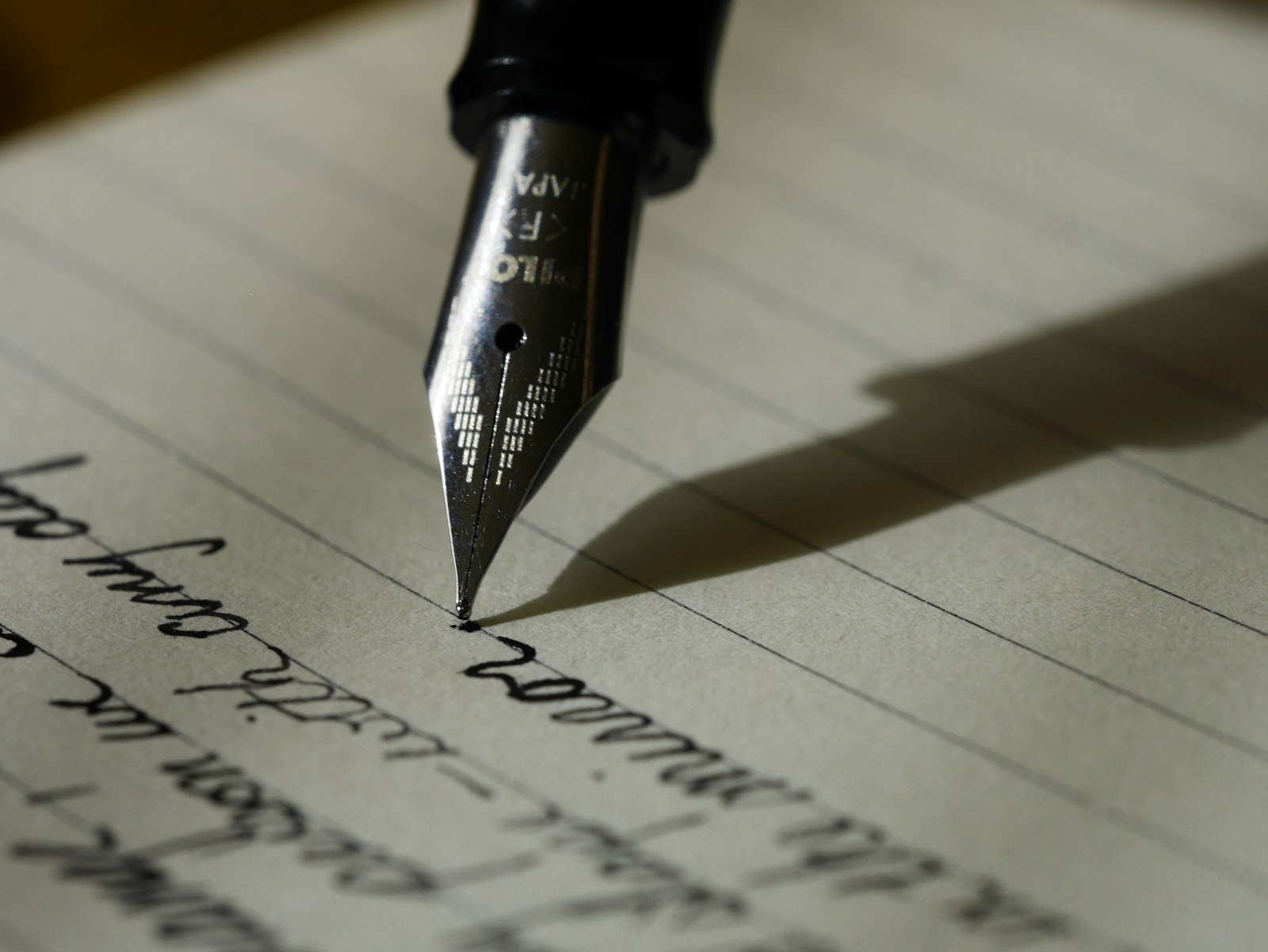 A fountain pen mid-stroke writing cursive script on lined paper