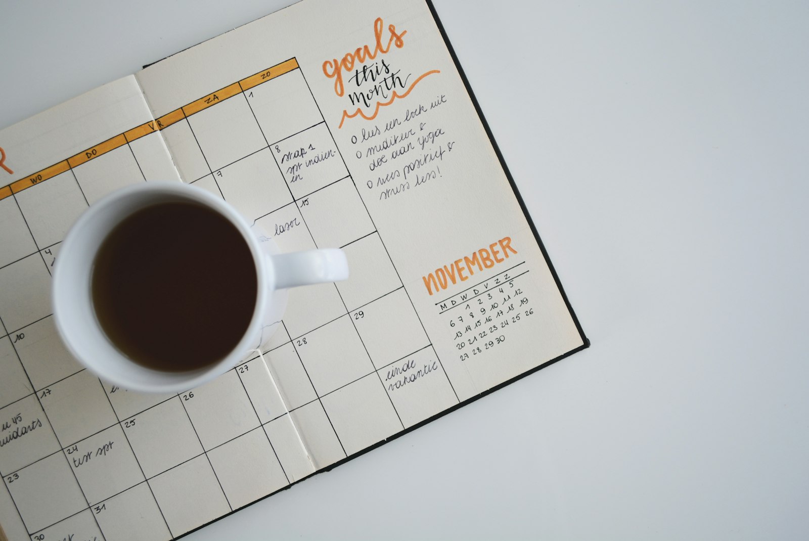 A planner showing a blank monthly calendar with handwritten goals beside a coffee mug